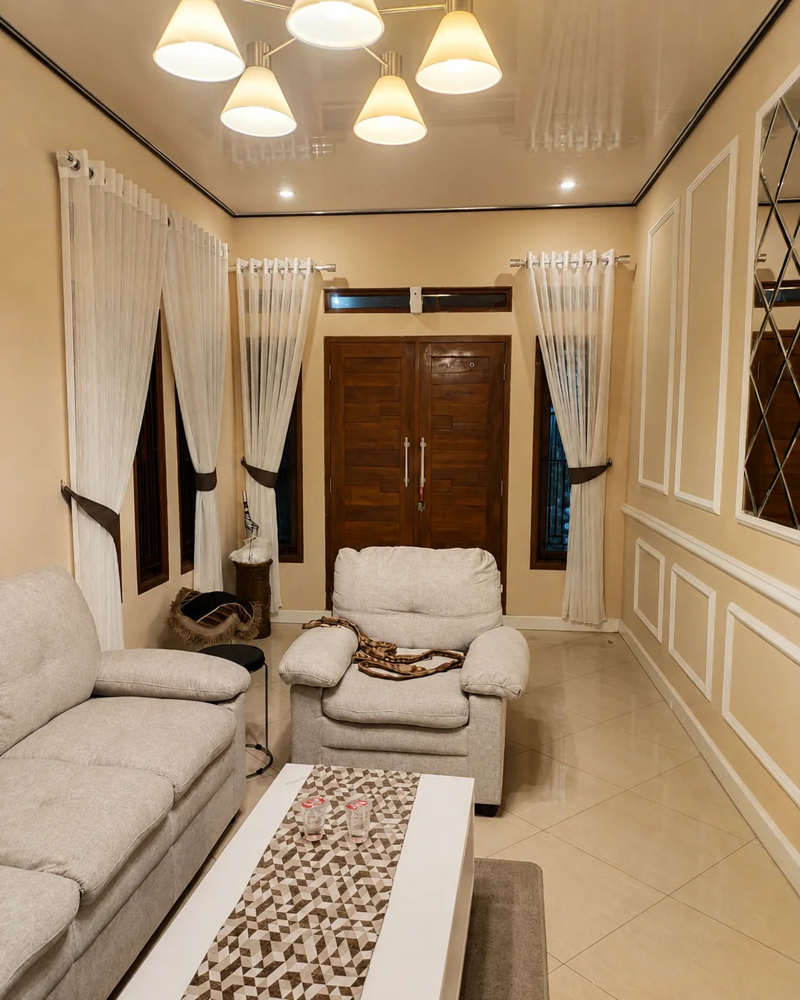 Vitrase putih terpasang pada beberapa jendela di ruang tamu dengan interior bernuansa hangat